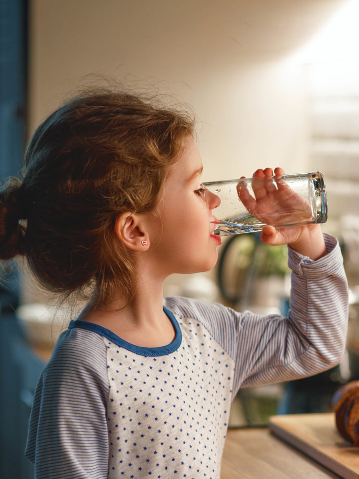 child girl is drinking water in the kitchen at home