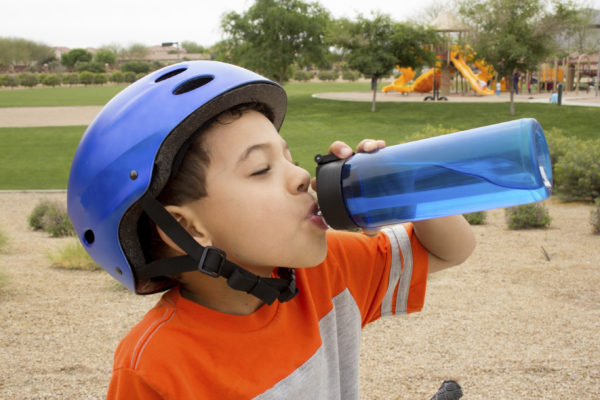 Boy in helmet drinks water to stay cool in heat wave