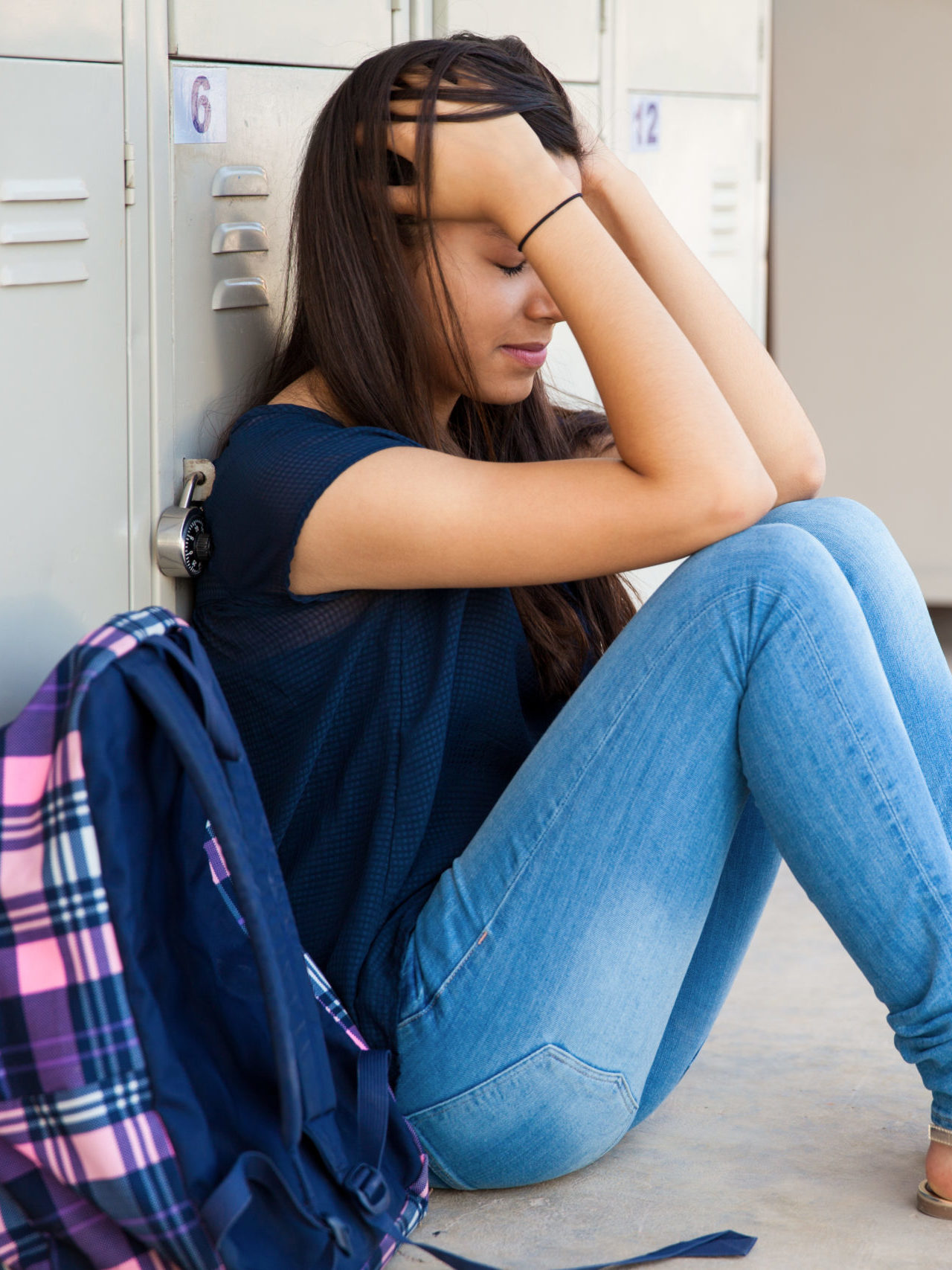 teen girl crying sitting on floor by lockers at school