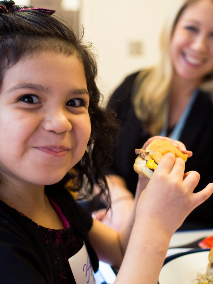 happy young girl eating a burger as a part of CHOC's Multidisciplinary Feeding Program