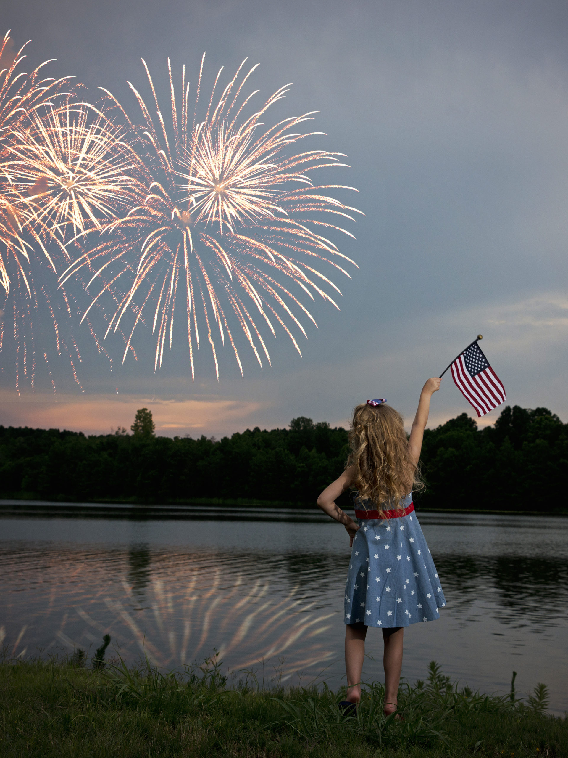 little girl watching fireworks display waving American flag