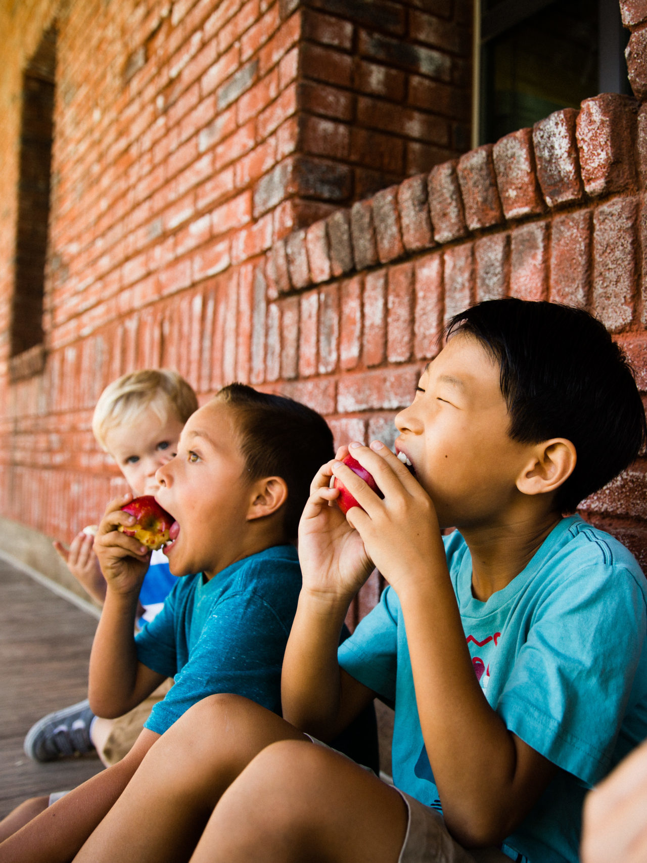 group of kids eating apples while sitting on the floor outside of school