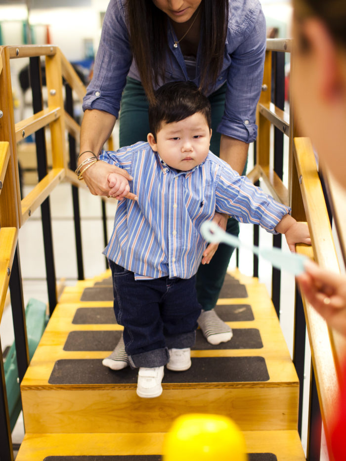 young toddler in physical therapy walking over wooden bridge with stairs