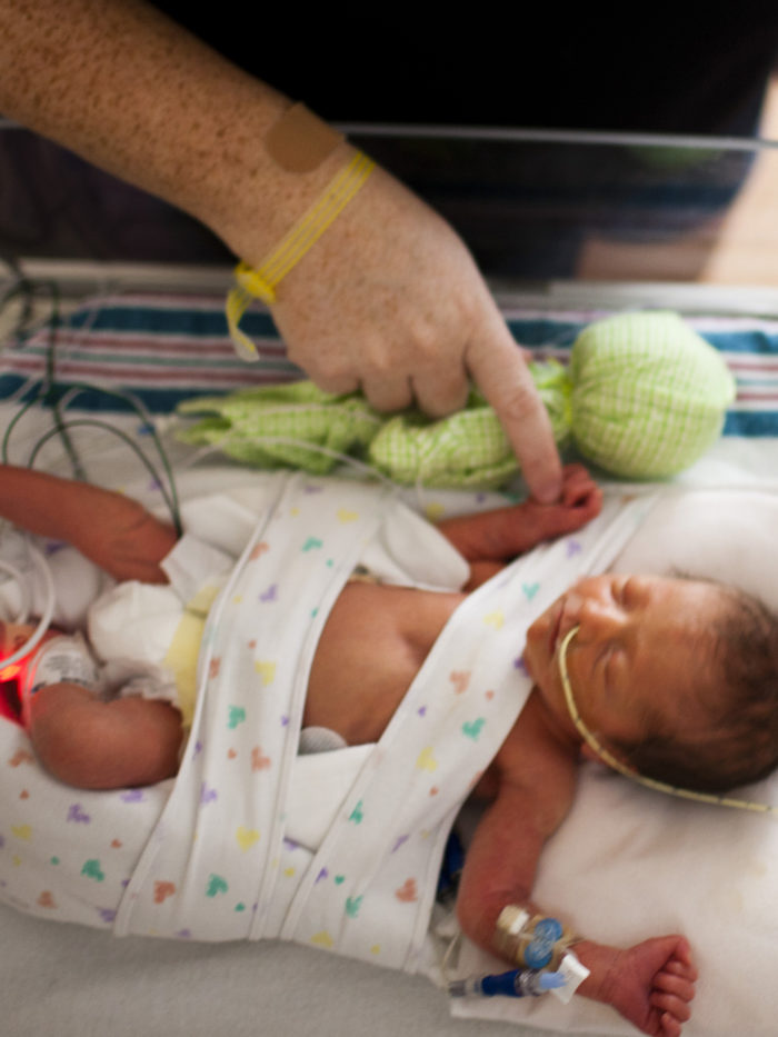baby asleep in the NICU while visitor touches her tiny hand