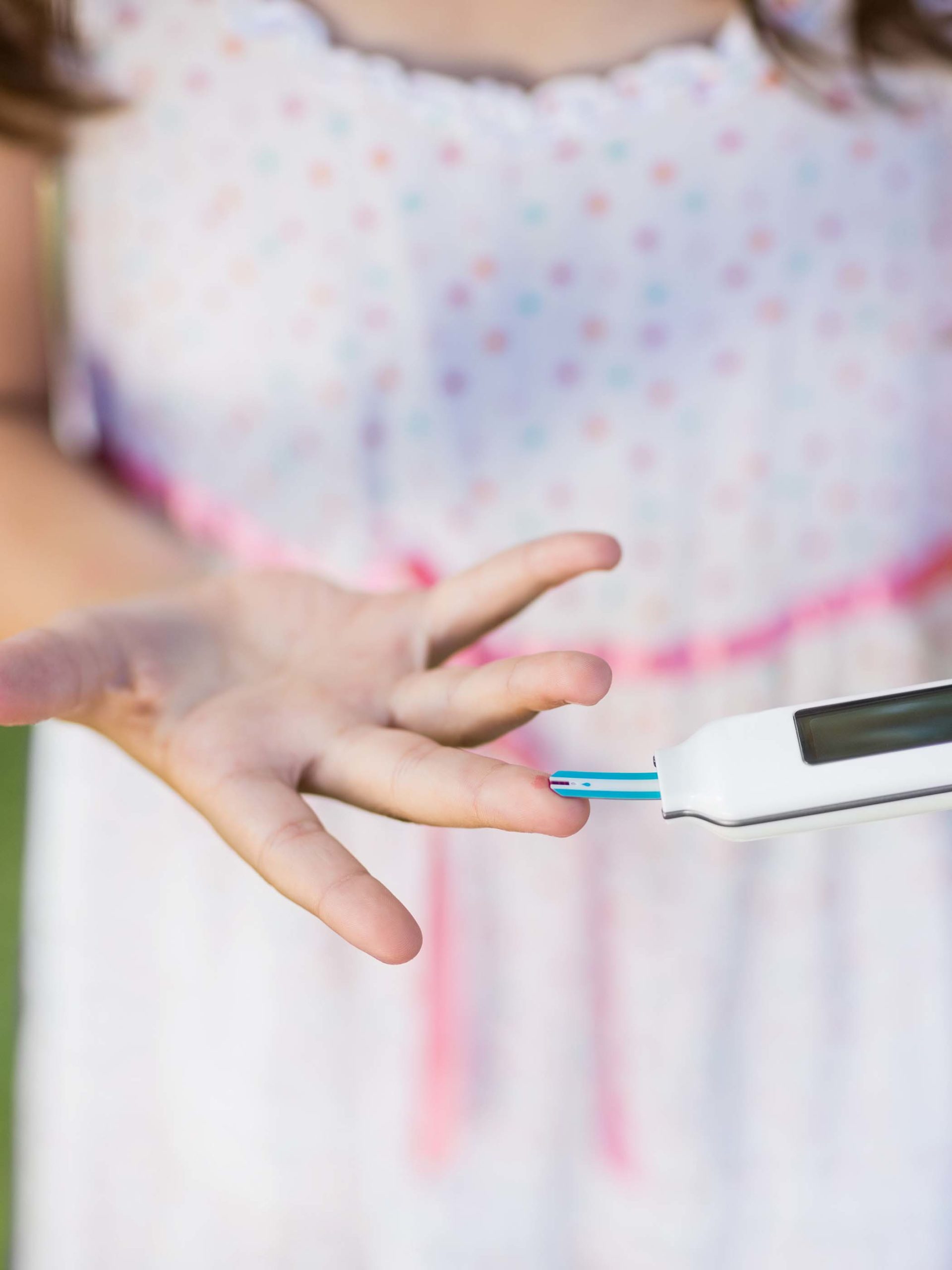 Close-up of diabetic girl using glucose meter in park to check blood sugar