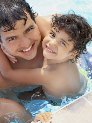 father holding his young son in the pool near the edge