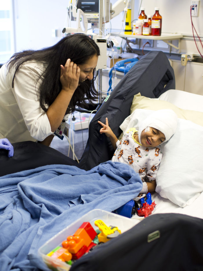 CHOC doctor Dr. Anjalee visiting patient in hospital bed making a peace sign