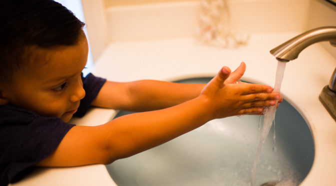 young boy stretching to reach the faucet to wash his hands