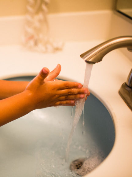 young boy stretching to reach the faucet to wash his hands