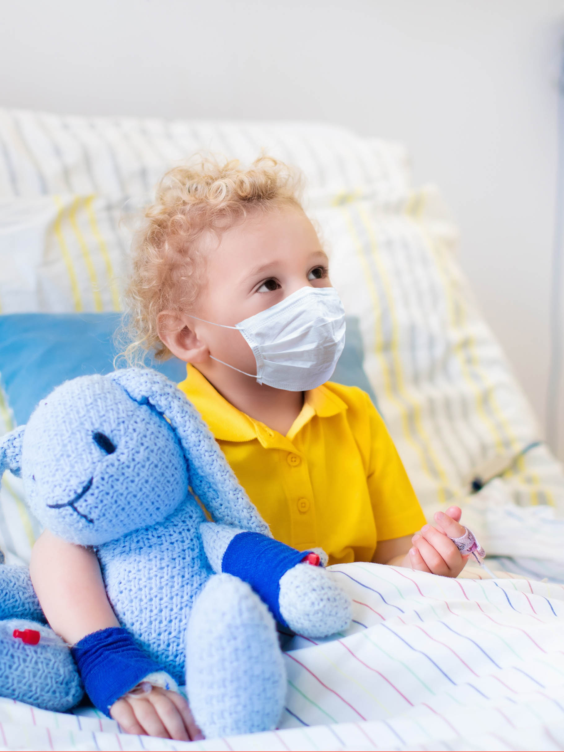 Little boy wearing face mask with his toy in bed in hospital room