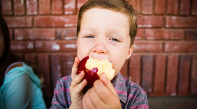 School boy taking a big bite into an apple