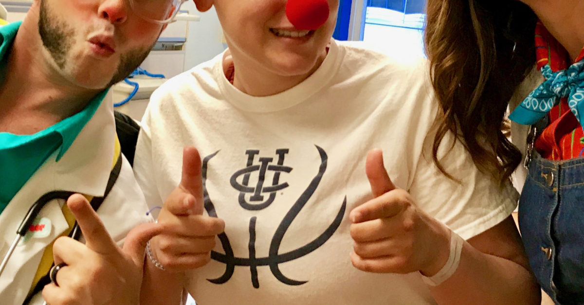 Sydney wearing a red nose posing with two clowns in her hospital room