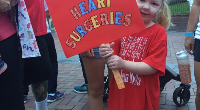 Emma at CHOC walk holding a sign that says "I've rocked 3 heart surgeries"