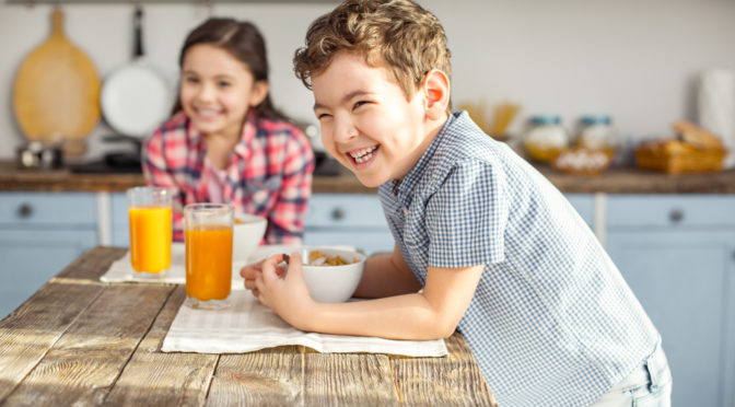 Siblings eating breakfast together in kitchen