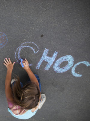 Young girl writing CHOC on the floor with chalk