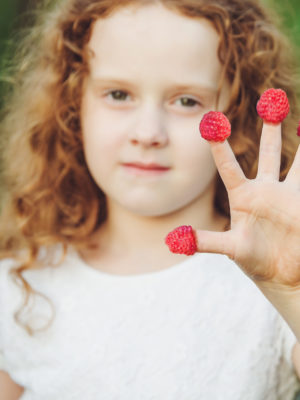 young girl playing with raspberries on her fingers