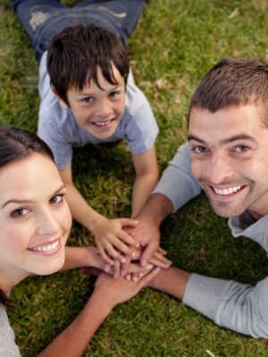 Happy parents and kid lying on grass with hands together