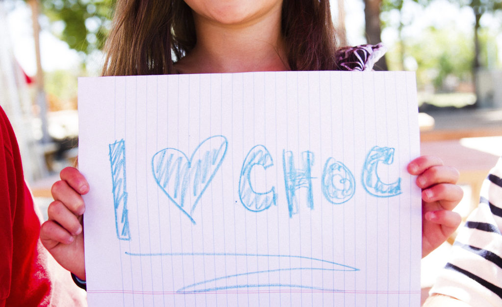 Little girl holding a sign she drew that says I heart CHOC