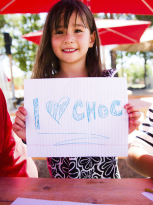 Little girl holding a sign she drew that says I heart CHOC