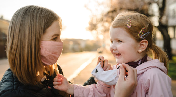 Mother helping her daugher put on a mask
