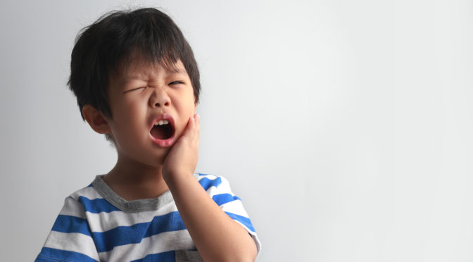young boy holding his face in pain because he has a tooth ache