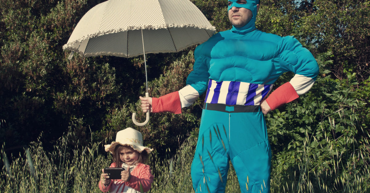 Man dressed as a super hero is protecting a little girl with umbrella.