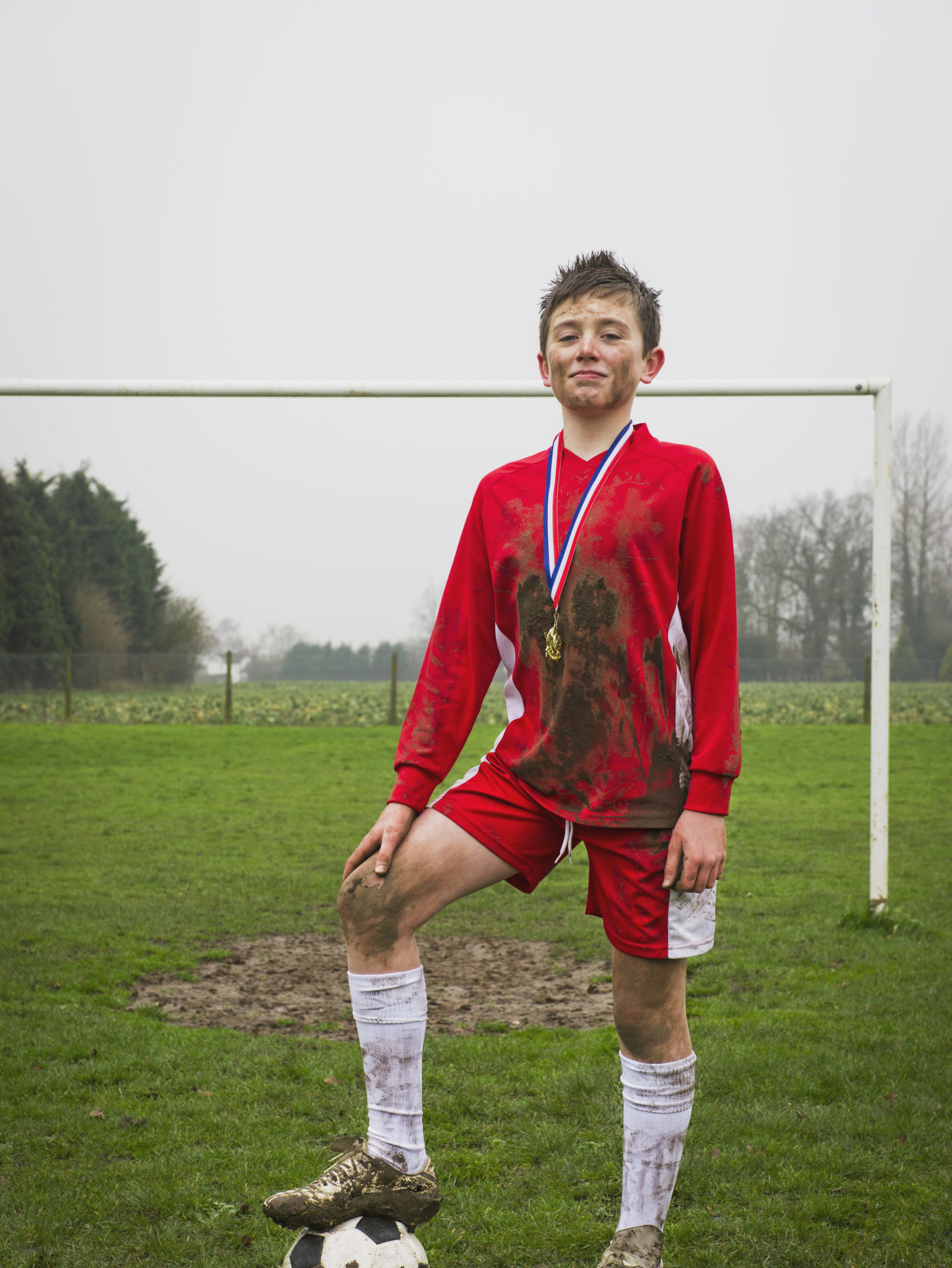 Young teen boy in soccer uniform covered in dirt with a medal