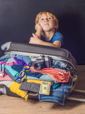 young boy with overflowing suitcase thinking about trip