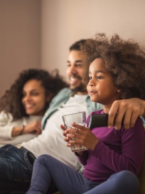 mom, dad and daughter watching TV together on couch