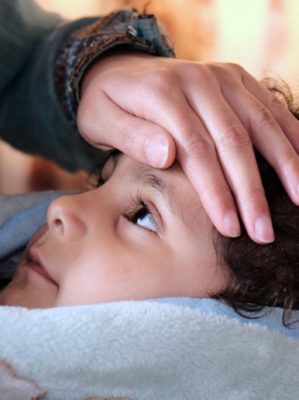 mom putting her hand on sick son's forehead to check his temperature