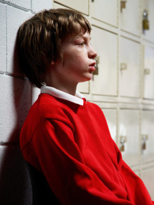 Schoolboy sitting in corridor leaning on wall next to lockers