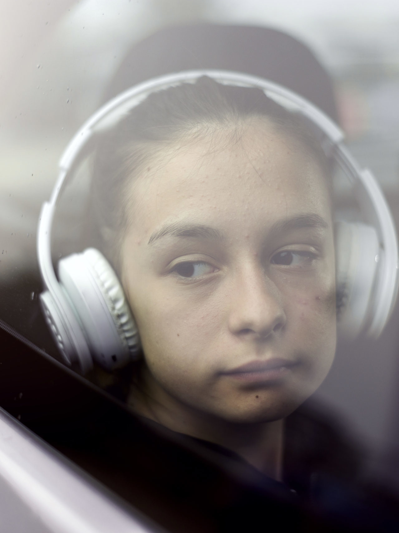 Sad teenager girl inside a car with white headphones on