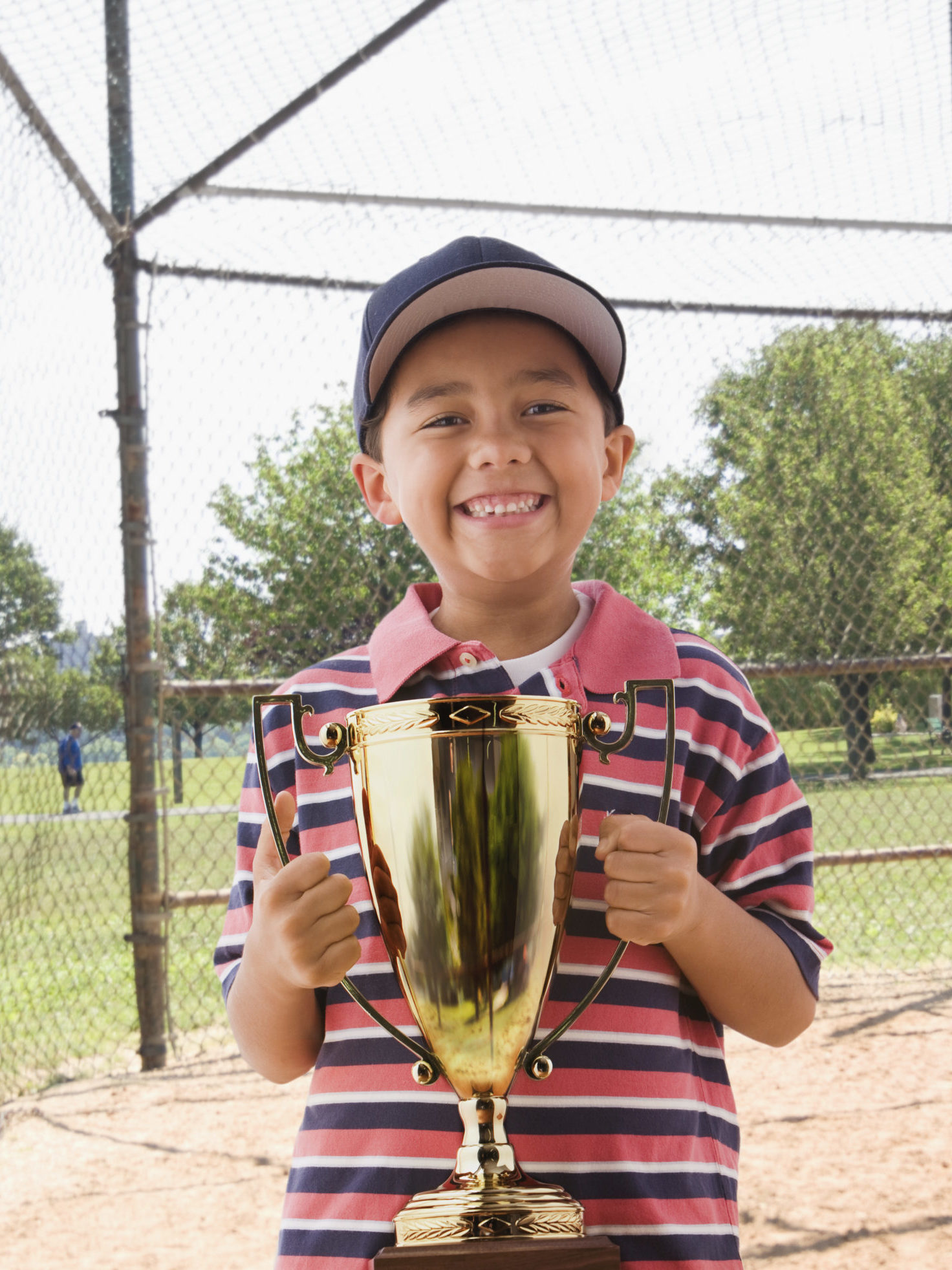 young boy on baseball field holding large trophy