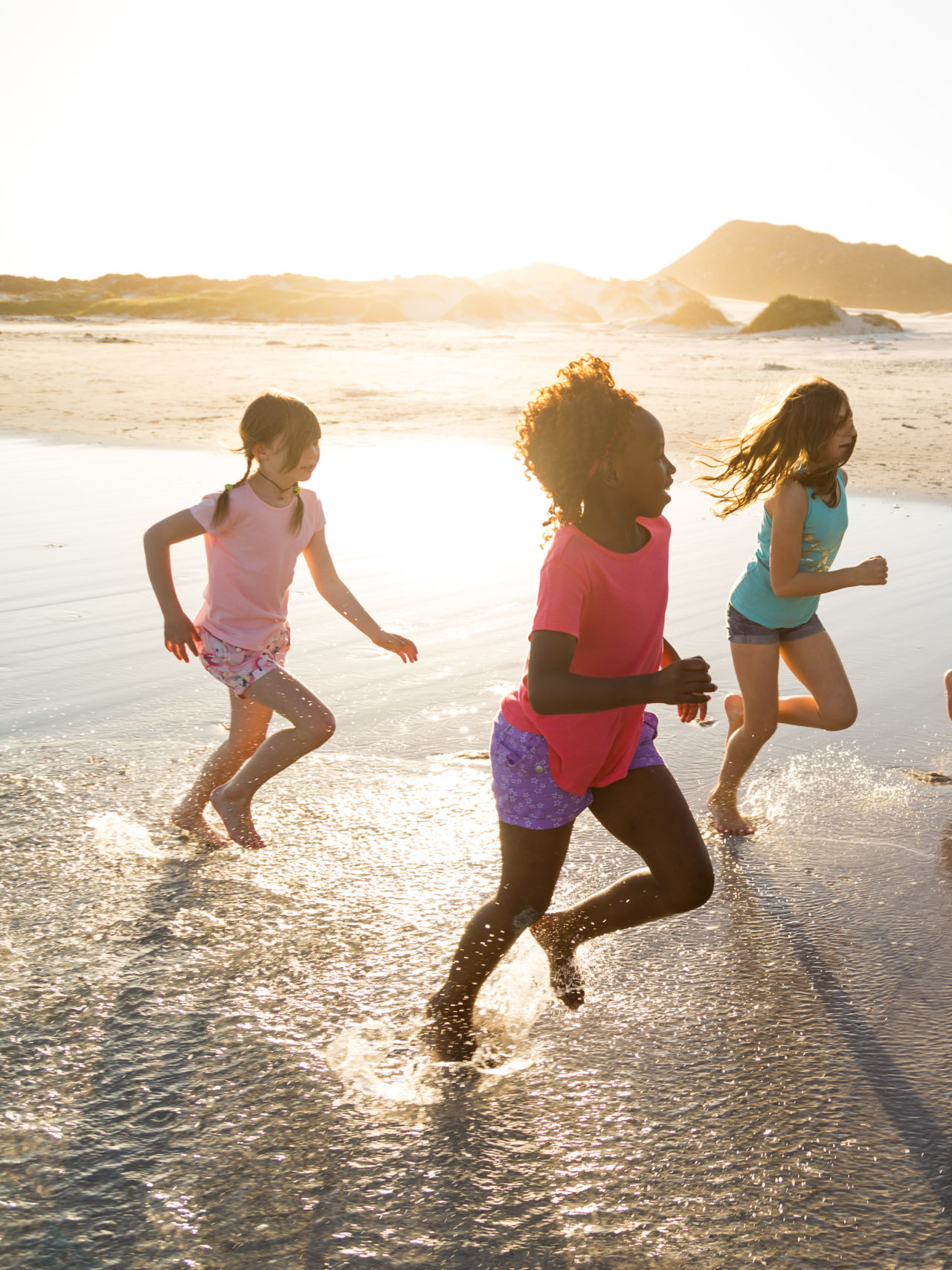 Group of children playing and running together on a beach at sunset