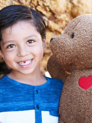 little boy smiling at the camera with CHOC teddy bear