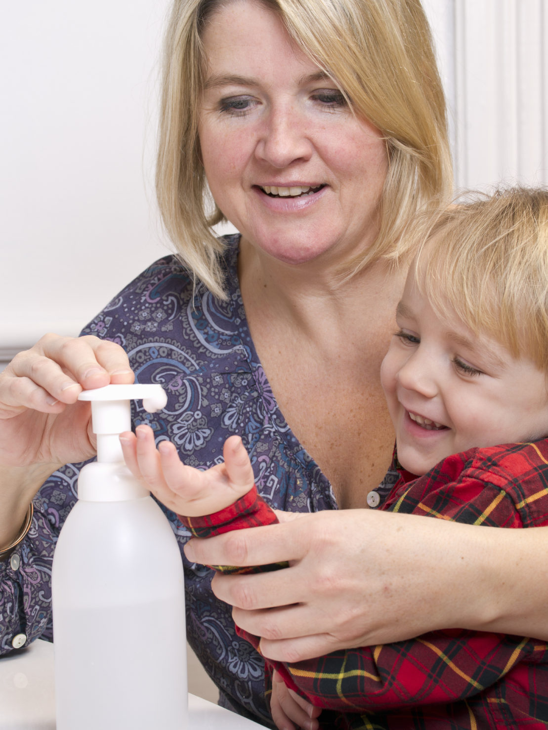 Mom helping her son disinfect his hand with bottle of sanitizer