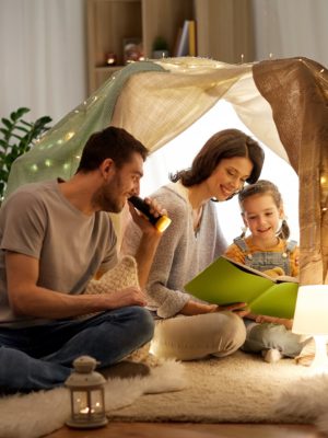 mom, dad and daughter reading a story in a pillow fort