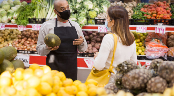 Store employee helping girl choosing fruit in supermarket.