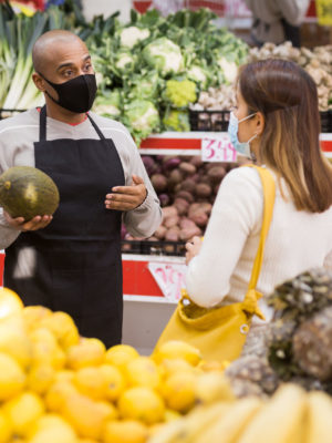 Store employee helping girl choosing fruit in supermarket.