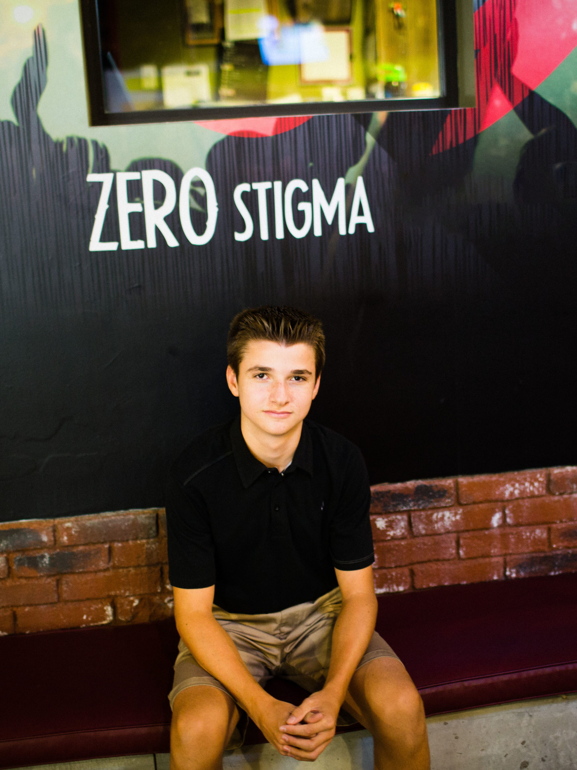 teen boy sitting in front of sign that says "Zero stigma"