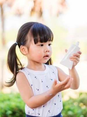 little girl with bottle of sunscreen putting it on