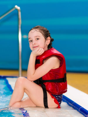 happy little girl in a red vest sitting on the steps of the pool in the water Park