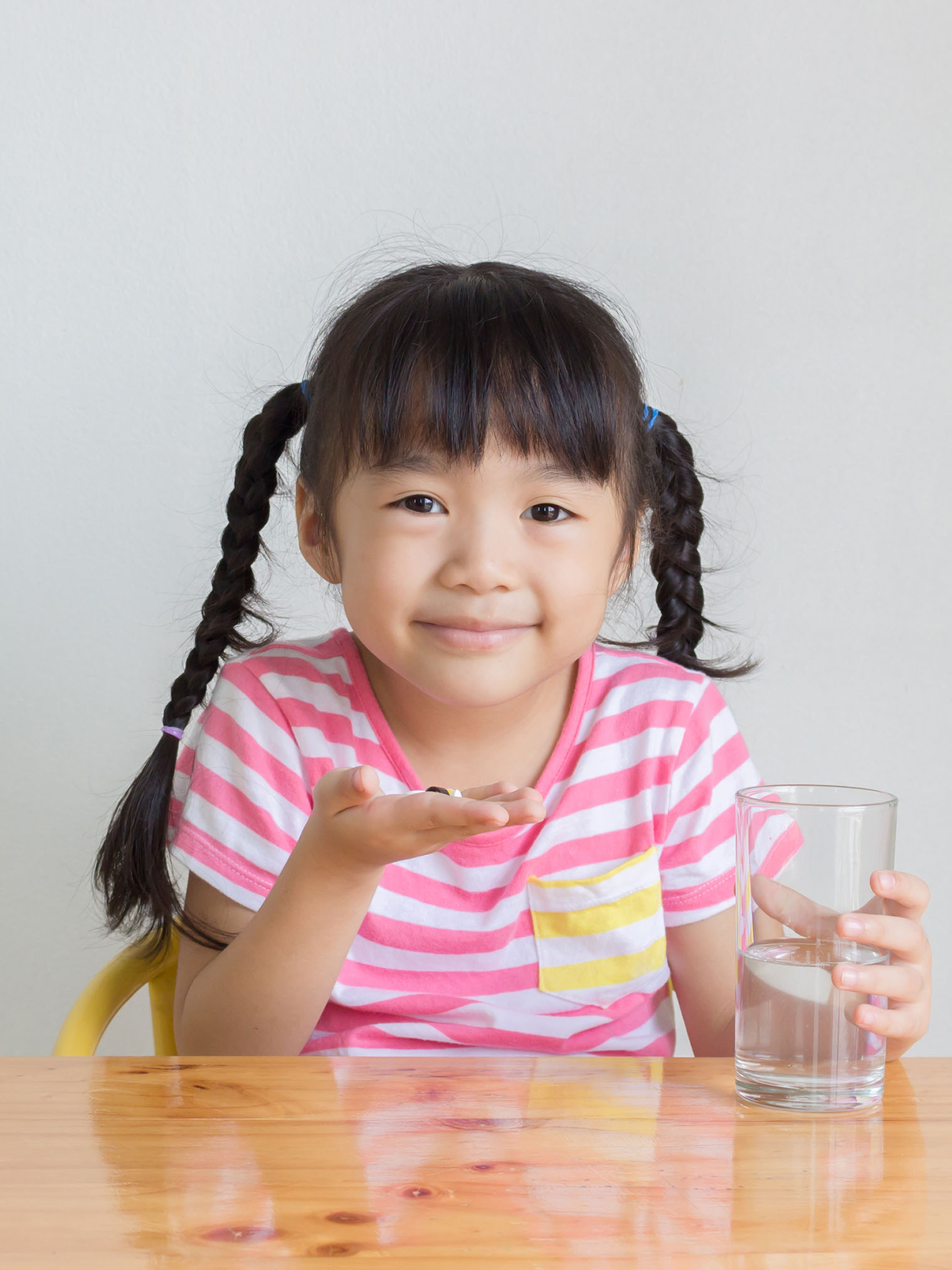 Little girl smiles while holding medication with a glass of water besides her.