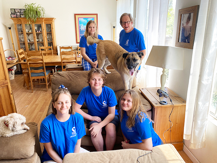 Family in matching CHOC shirts pose for a photo in their living room
