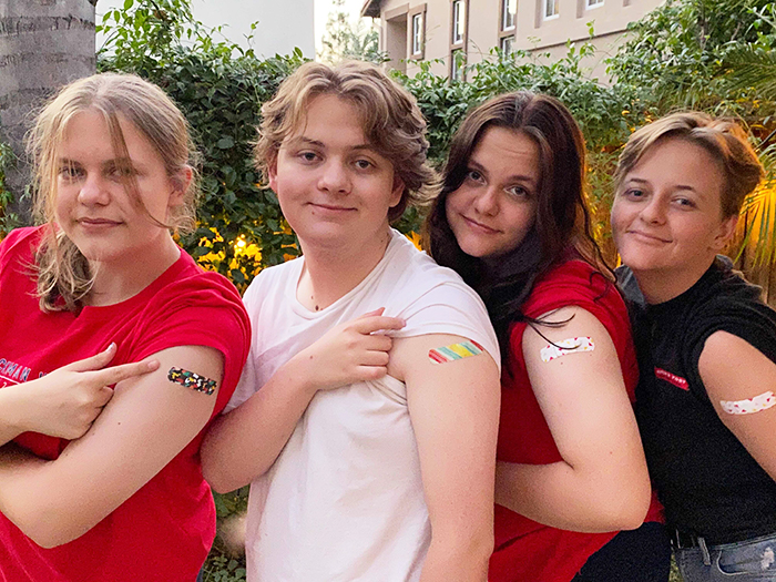 4 teenagers pulling up their sleeves to show bandages on their upper arm 