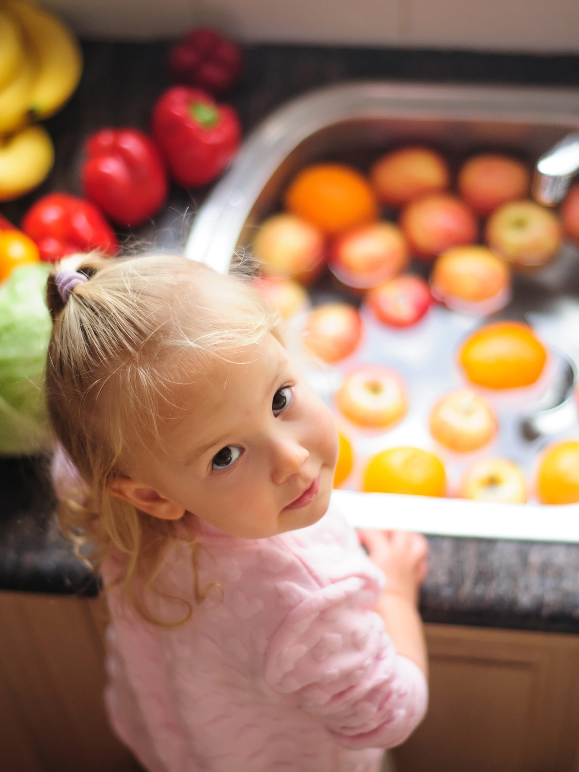 Little girl looks up with sink of veggies behind her