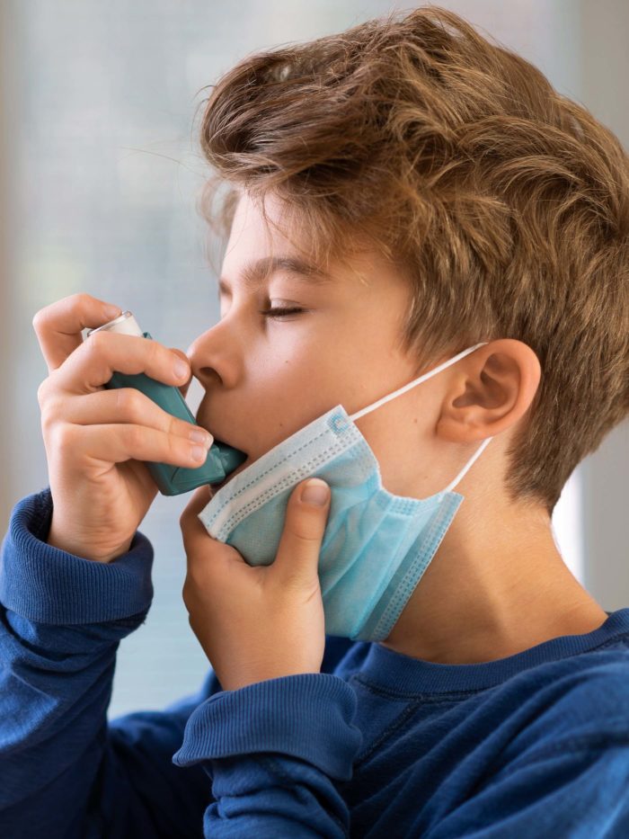 Boy pulls mask down to use asthma inhaler