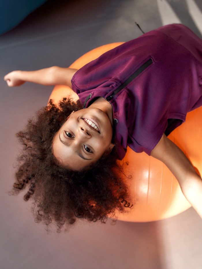 child playing on exercise ball stretching her back