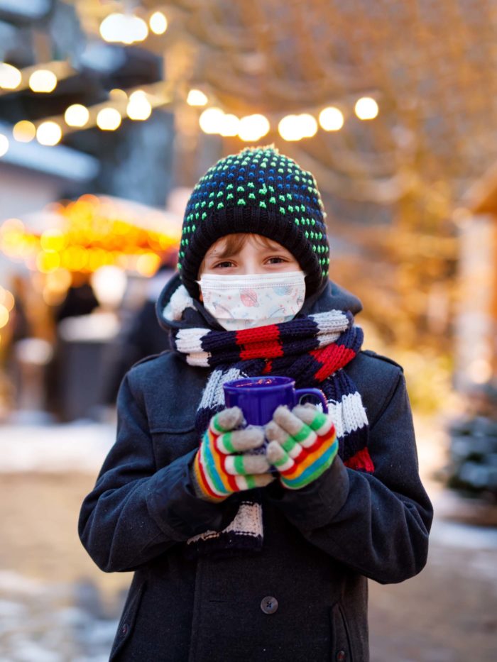 boy holding mug smiles with mask on in the cold weather outside
