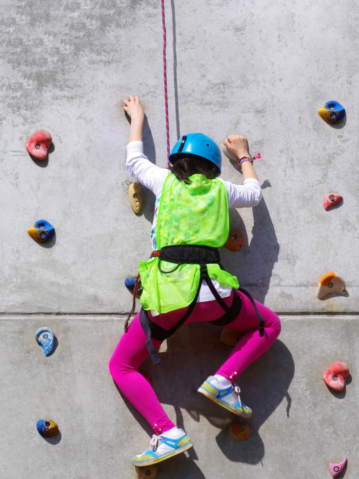 young girl climbing rock wall at gym in safety gear
